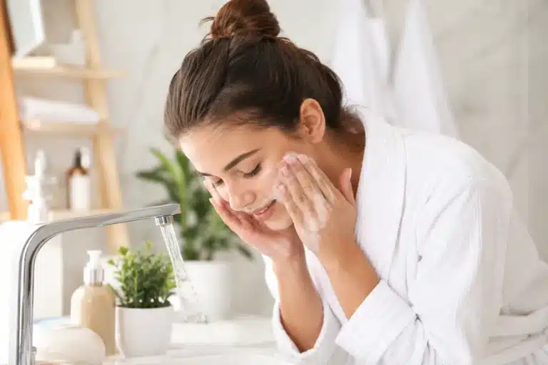 Femme appliquant un gel nettoyant visage moussant devant son lavabo